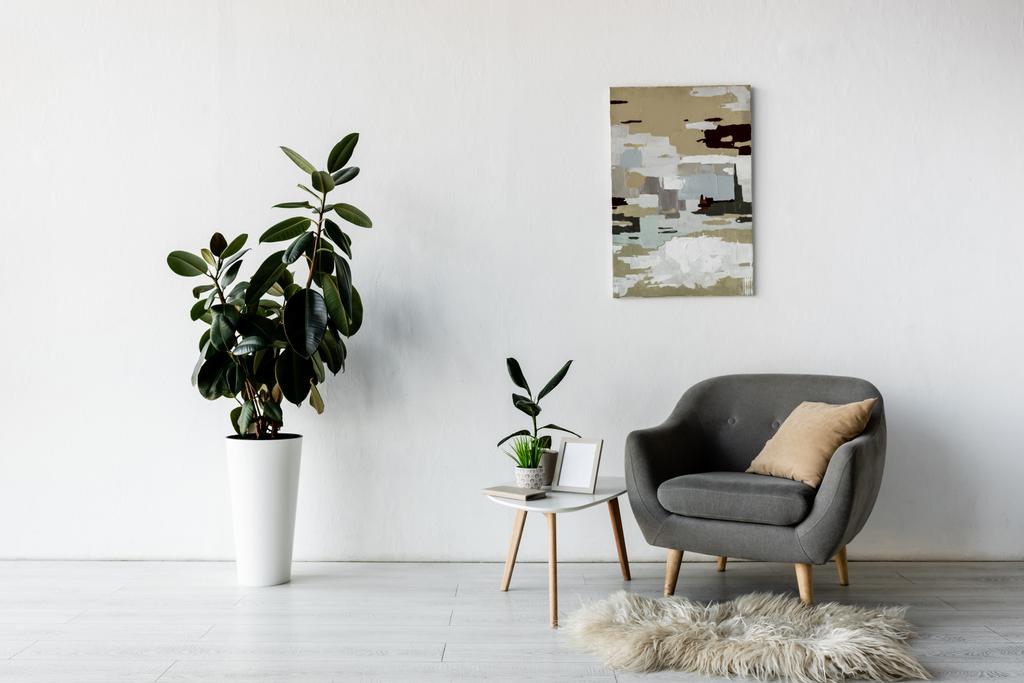 szary fotel przy stoliku z zielonymi roślinami i ramą w nowoczesnym salonie  - Zdjęcie, obraz