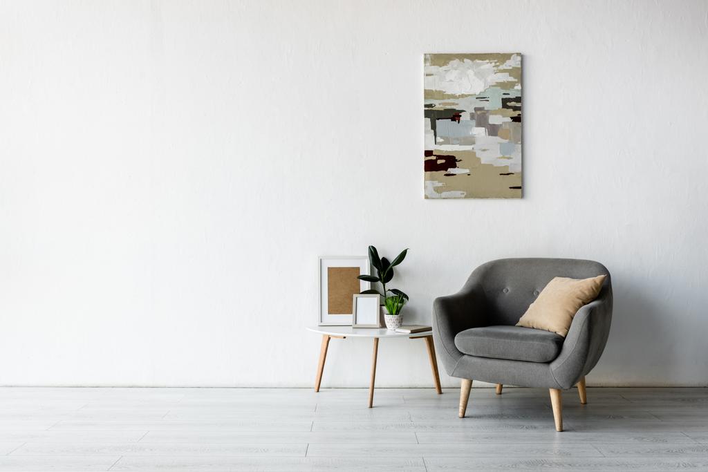 wygodny fotel przy stoliku z zielonymi roślinami i ramami w nowoczesnym salonie  - Zdjęcie, obraz