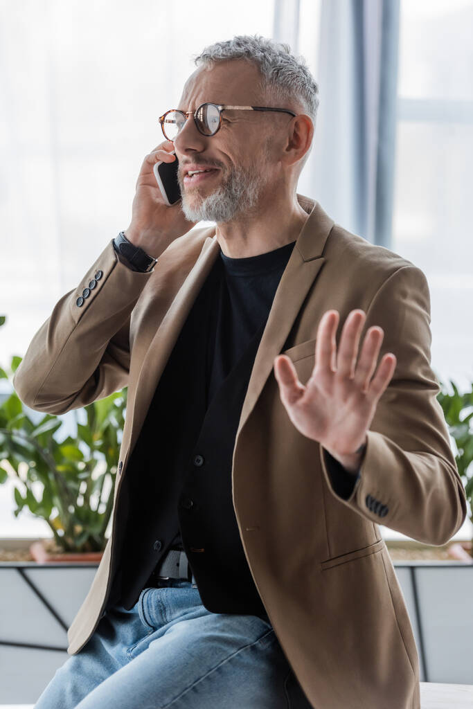 selective focus of bearded businessman in glasses gesturing and talking on smartphone  - Photo, Image
