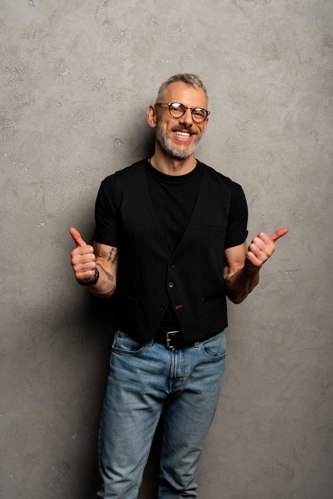 Fröhlicher Mann mit Brille zeigt Daumen hoch auf grau  - Foto, Bild