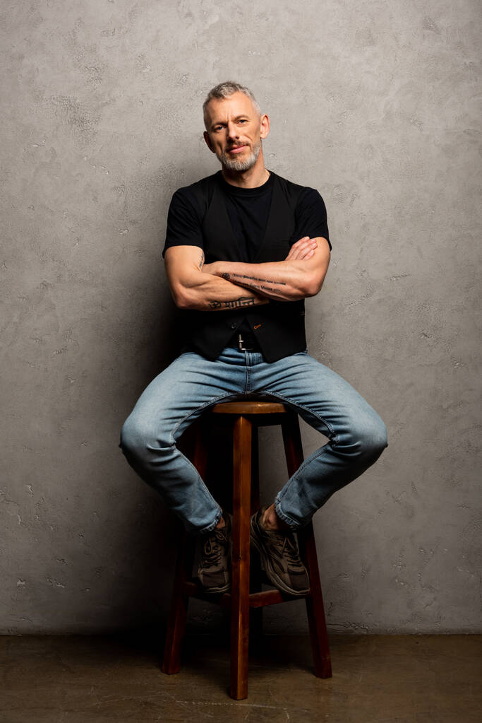 uomo barbuto con braccia incrociate seduto su sgabello grigio
  - Foto, immagini