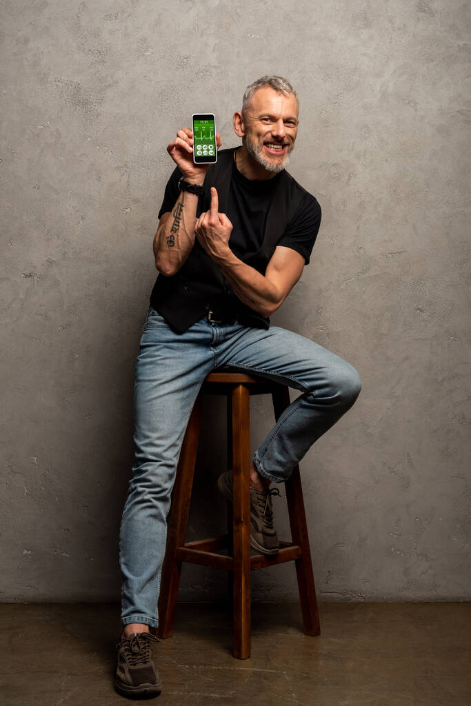 щасливий чоловік з татуюванням, вказуючи пальцем на смартфон з медичним додатком на сірому
  - Фото, зображення