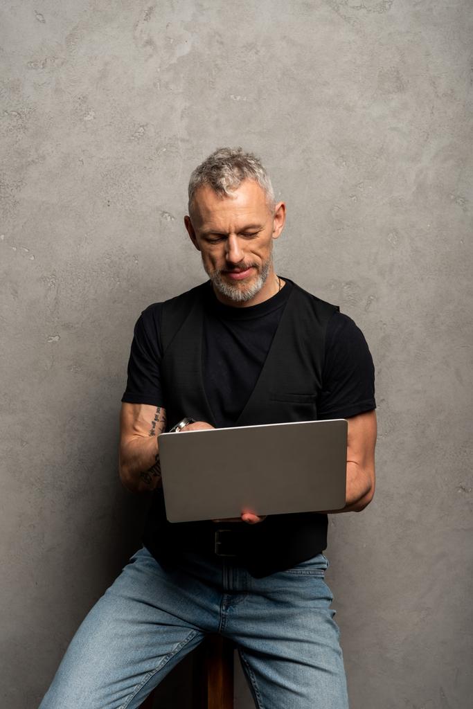 красивий чоловік з татуюванням використовує ноутбук на сірому
 - Фото, зображення