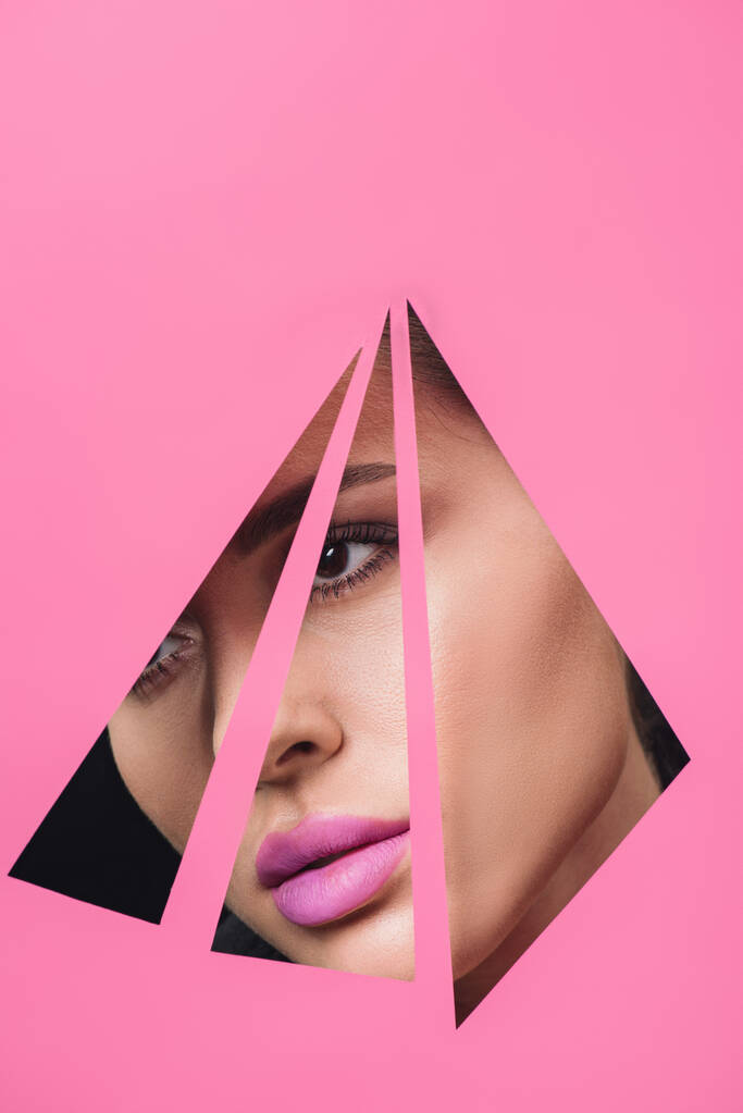 Vrouw met roze lippen kijkend over driehoekige gaten in papier - Foto, afbeelding