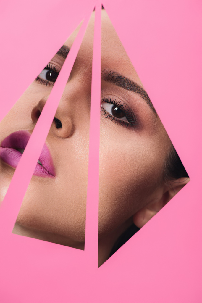 Όμορφη γυναίκα με καπνιστά μάτια και ροζ χείλη κοιτάζοντας σε τριγωνικές τρύπες στο χαρτί  - Φωτογραφία, εικόνα