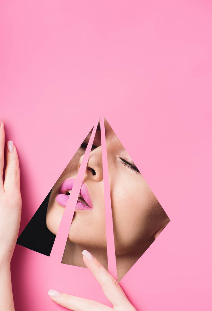 Woman with pink lips and closed eyes across triangular holes touching paper on black  - Photo, Image