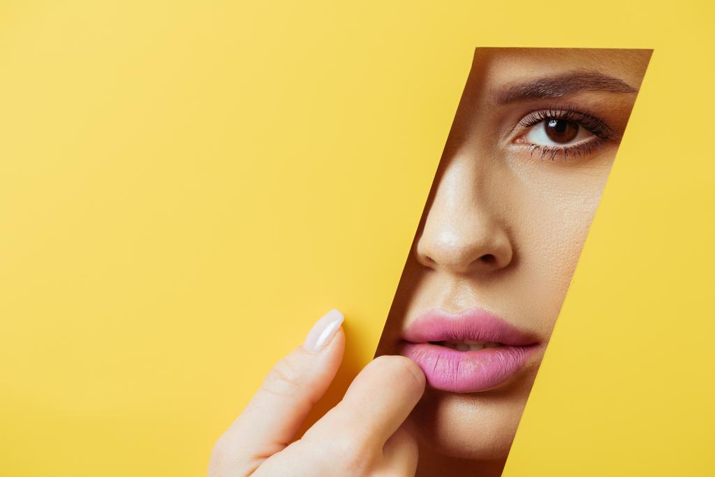 Vrouw met roze lippen kijkend naar camera over vierhoekig gat en het aanraken van geel papier - Foto, afbeelding