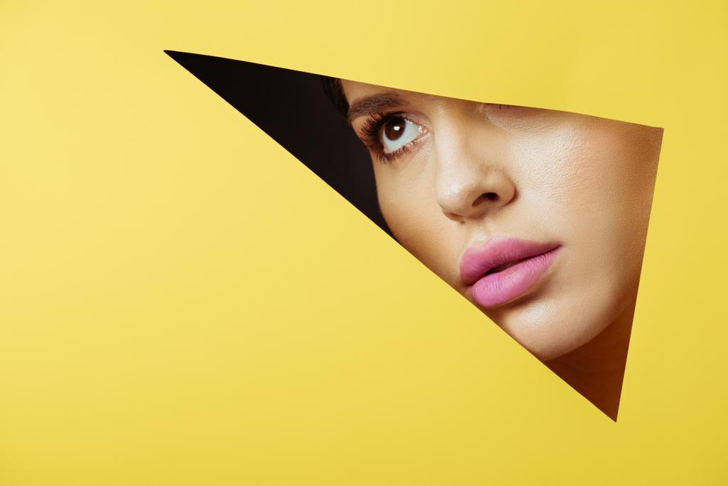 Femme aux lèvres roses regardant à travers un trou triangulaire en papier jaune sur fond noir
 - Photo, image