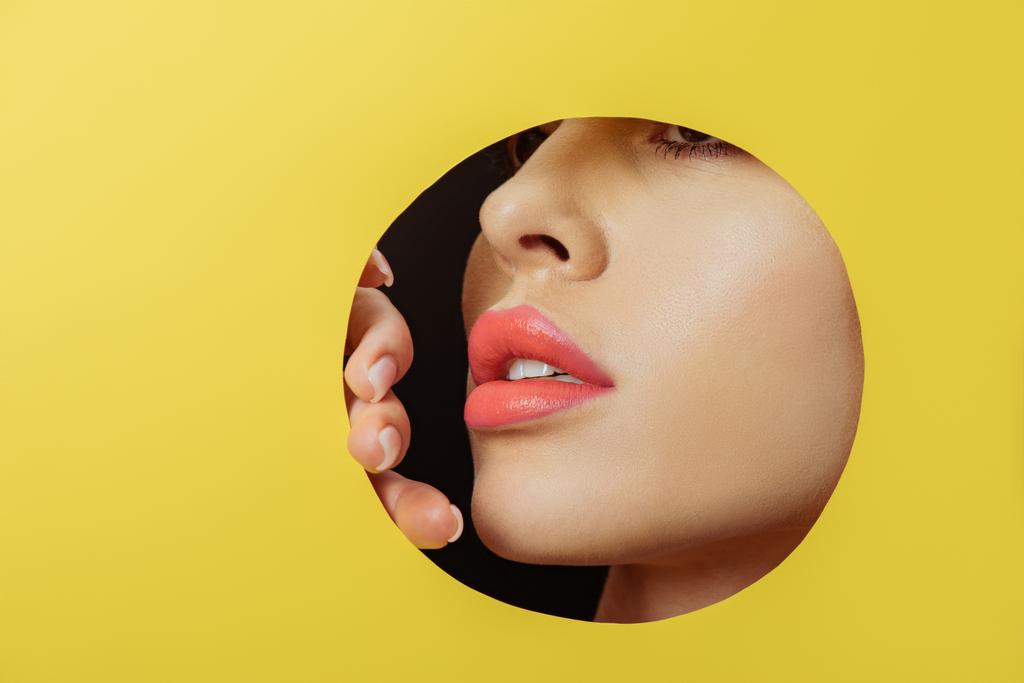 Face feminina com lábios de coral e dedos em buraco redondo em papel amarelo em preto
 - Foto, Imagem