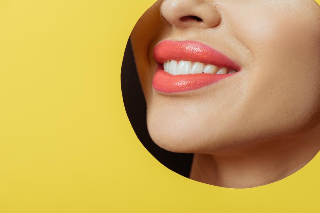 Vista recortada de mujer con labios de coral sonriendo en agujero redondo en papel amarillo sobre negro
  - Foto, imagen