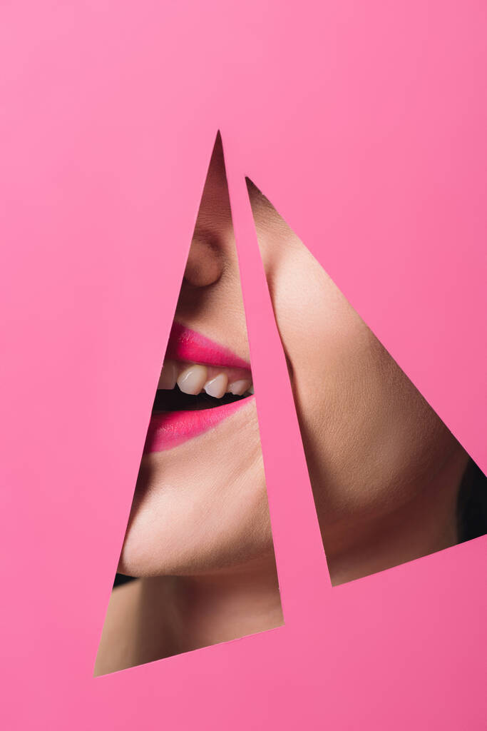 Rajatut näkymä nainen vaaleanpunainen huulet hymyillen kolmion reikiä paperilla
  - Valokuva, kuva