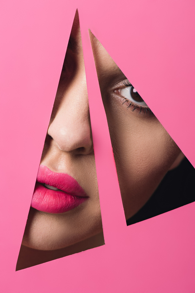 Chica con labios rosados mirando a la cámara a través de agujeros triangulares en papel sobre fondo negro
 - Foto, imagen