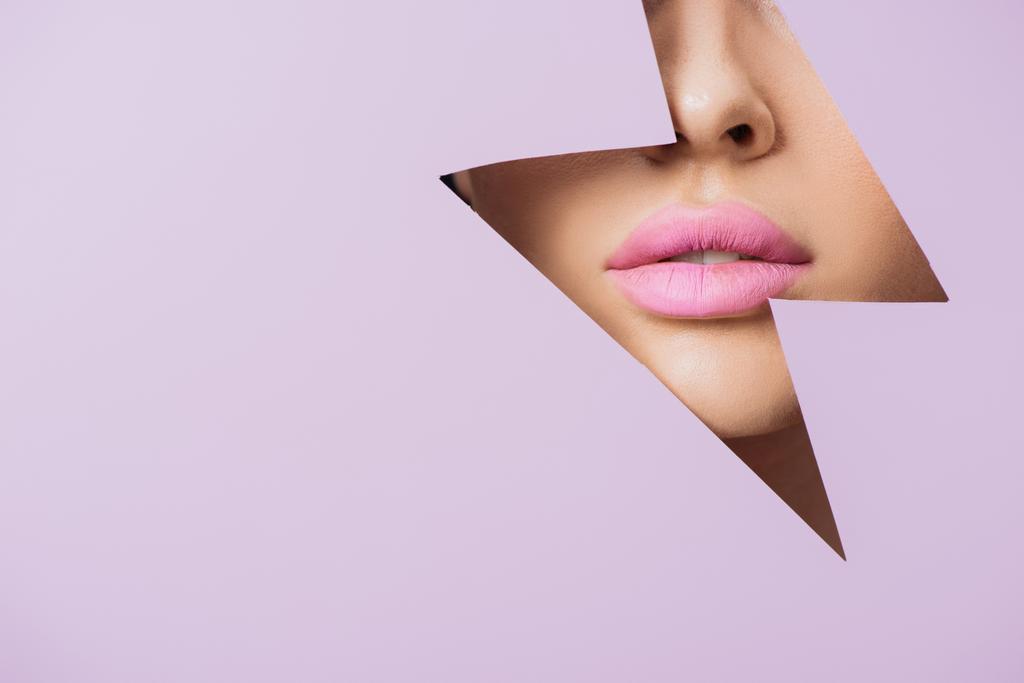 Gewassen gezicht van vrouwelijk gezicht met roze lippen in gat in violet papier - Foto, afbeelding