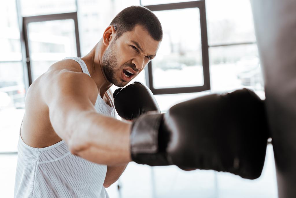 enfoque selectivo de deportista enojado en guantes de boxeo haciendo ejercicio con saco de boxeo
   - Foto, Imagen