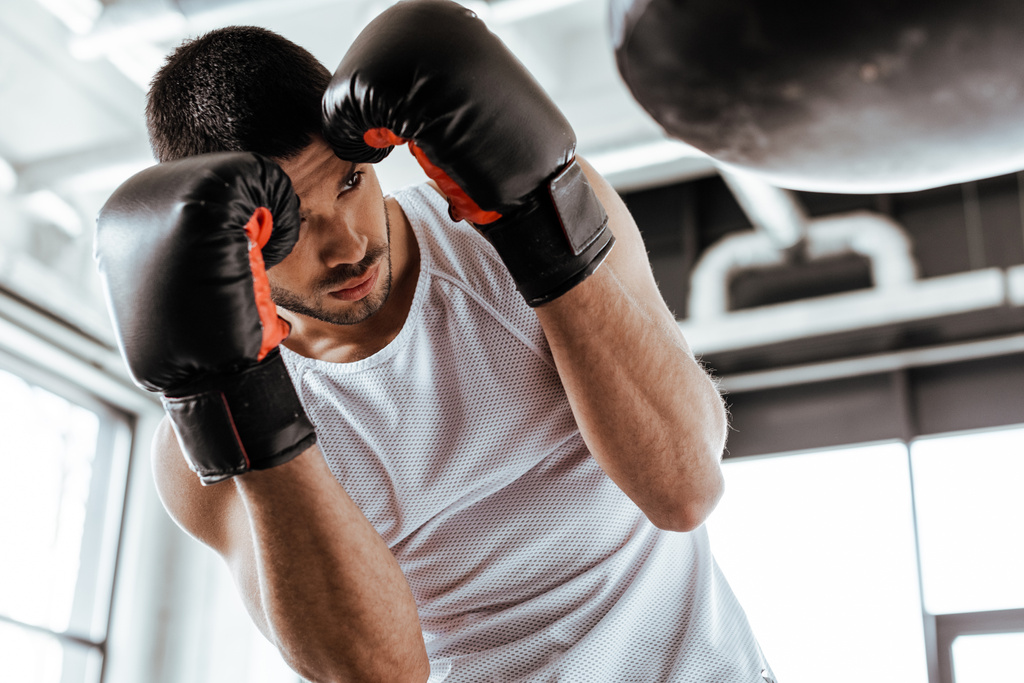 selective focus of sportsman in boxing gloves training with punching bag   - Photo, Image