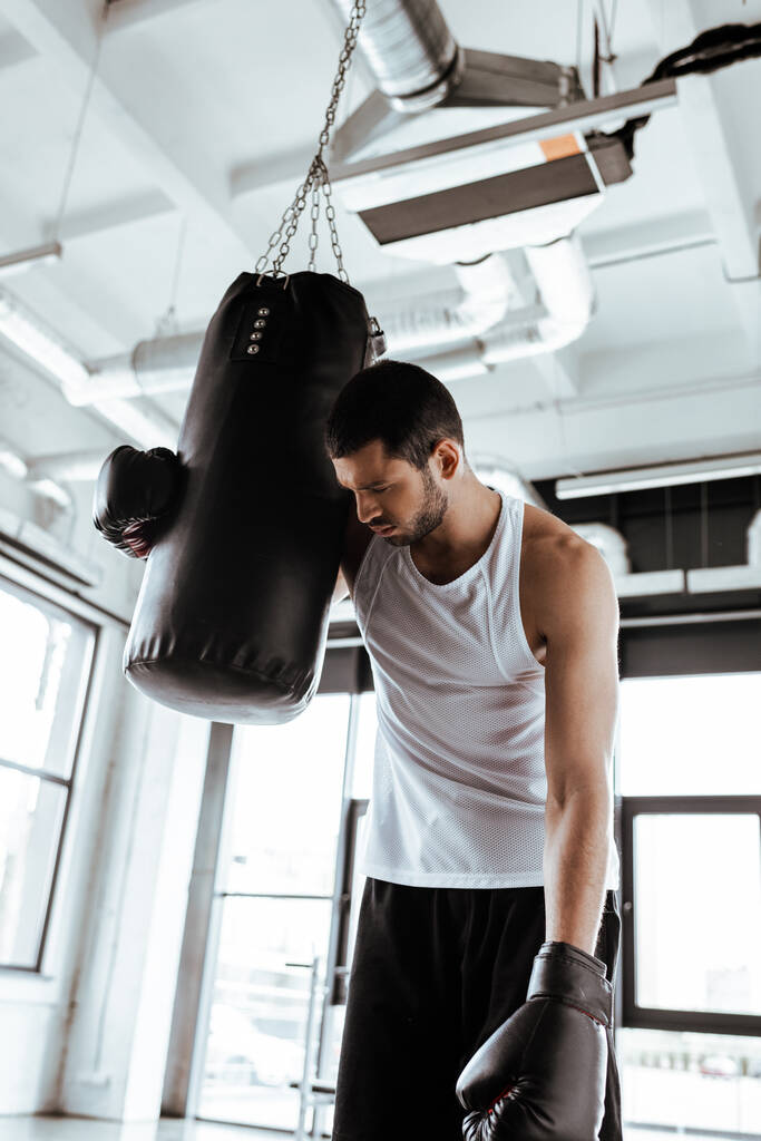 измученный спортсмен в боксёрских перчатках стоит рядом с боксёрской грушей
   - Фото, изображение