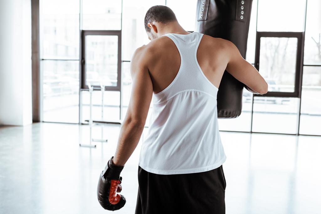 Rückansicht des Sportlers im Boxhandschuh, der Boxsack berührt   - Foto, Bild