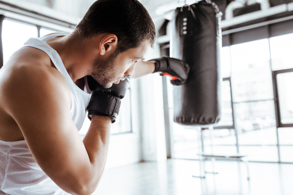 selective focus of athletic sportsman in boxing gloves training with punching bag - Photo, Image