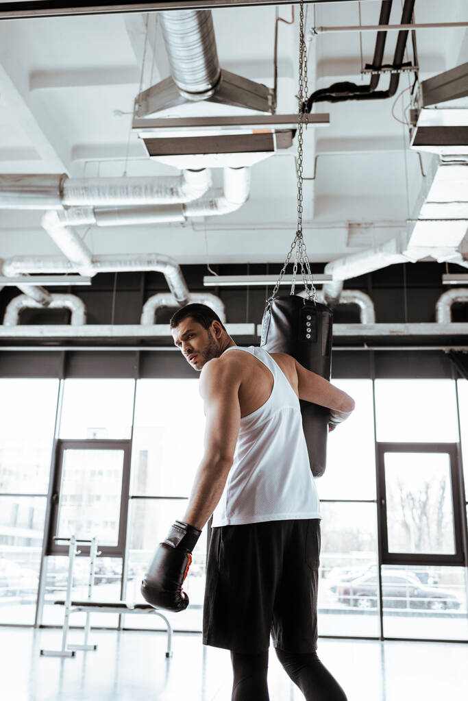 красивый спортсмен смотрит в камеру рядом с боксерской грушей
   - Фото, изображение
