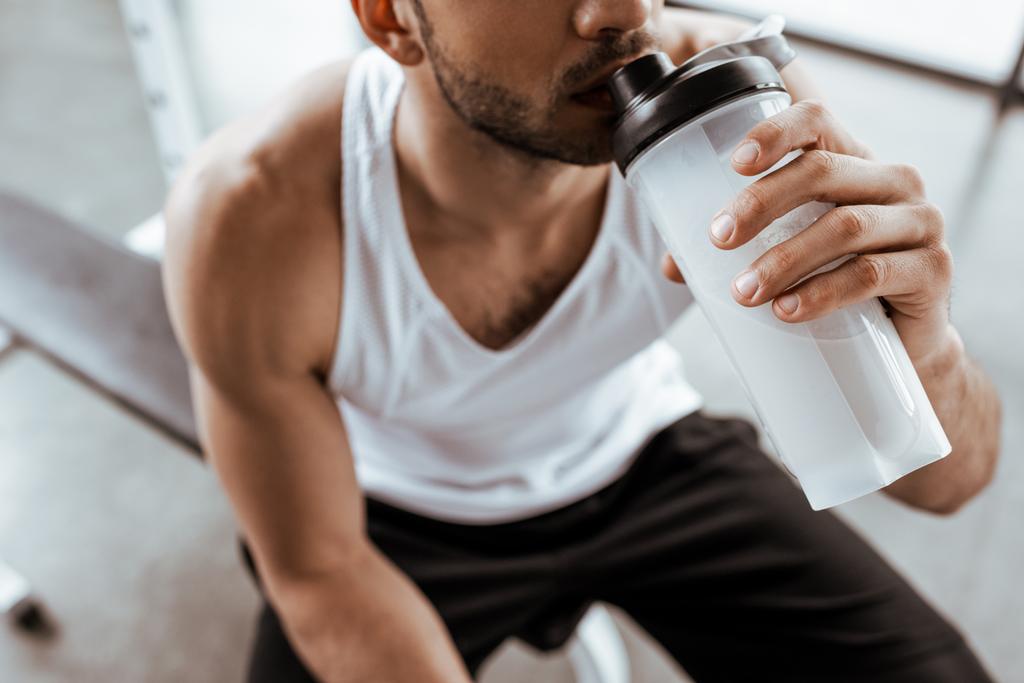 cropped view of sportsman drinking protein milkshake while holding sports bottle  - Photo, Image