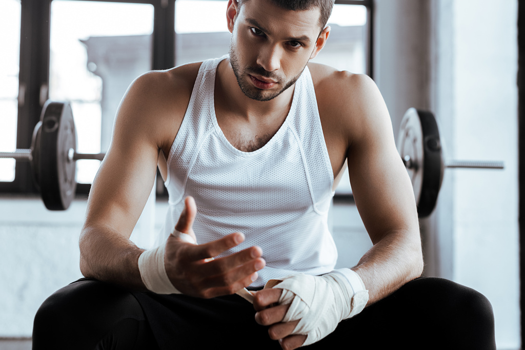 handsome sportsman wrapping hand in sports bandage and looking at camera - Photo, Image