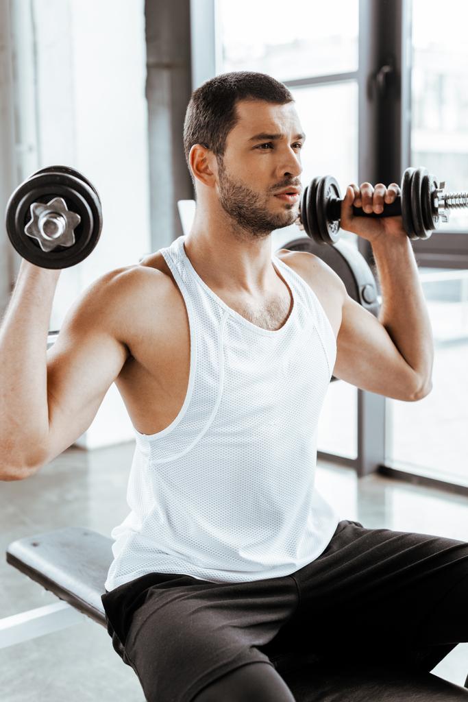 deportista atlético sosteniendo pesas mientras hace ejercicio en el gimnasio
   - Foto, imagen