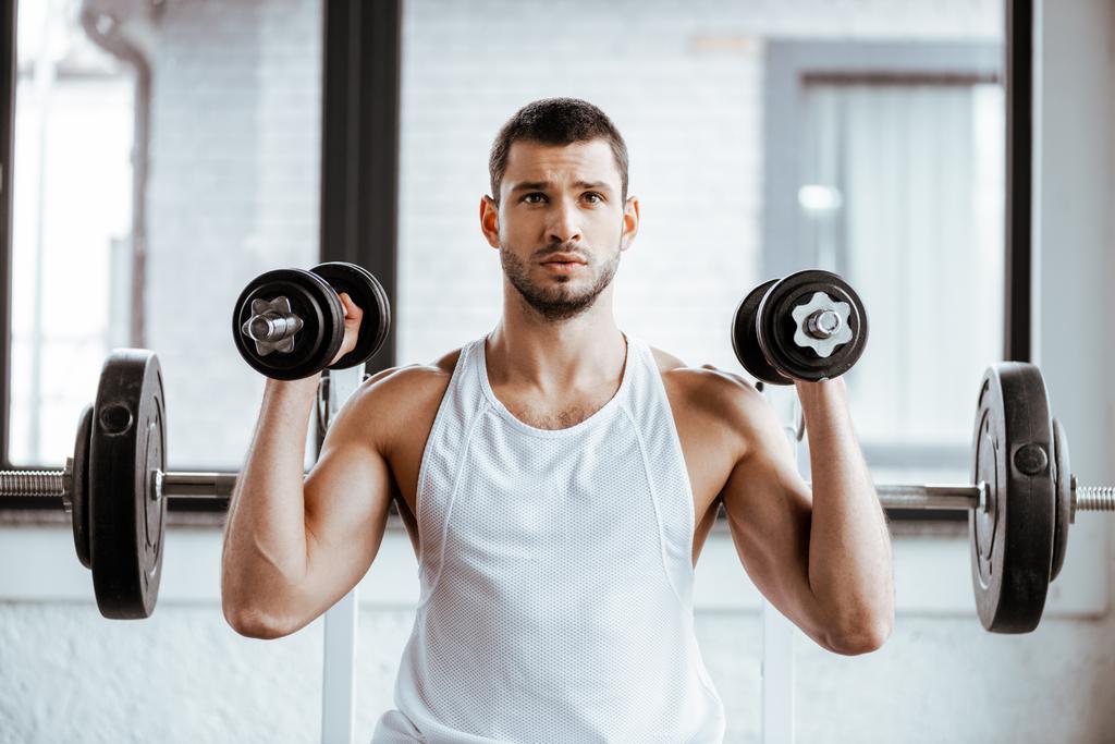 deportista atlético sosteniendo pesas mientras hace ejercicio en el gimnasio
   - Foto, Imagen