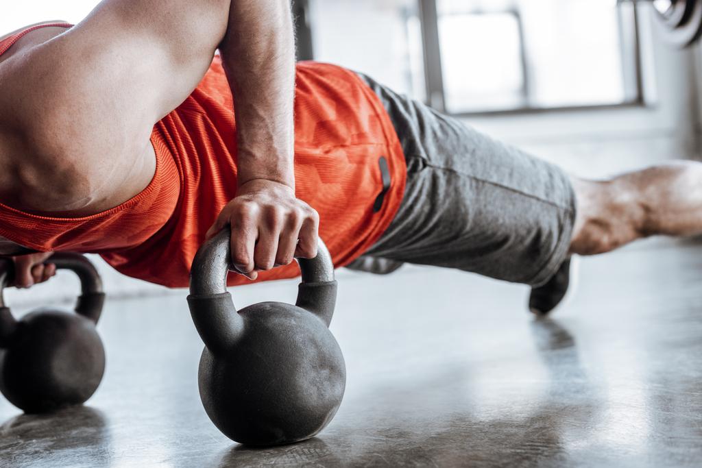 cropped view of athletic sportsman doing plank exercise with heavy dumbbells  - Photo, Image