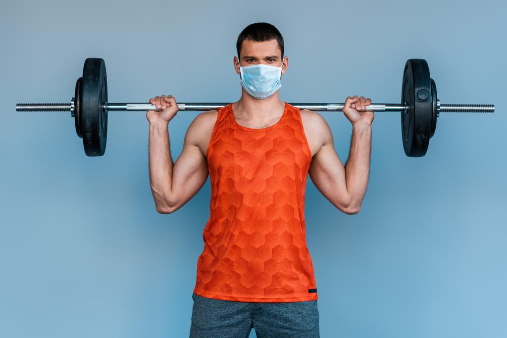 ブルーで隔絶されたバーベルで働く医療マスクのスポーツマン  - 写真・画像