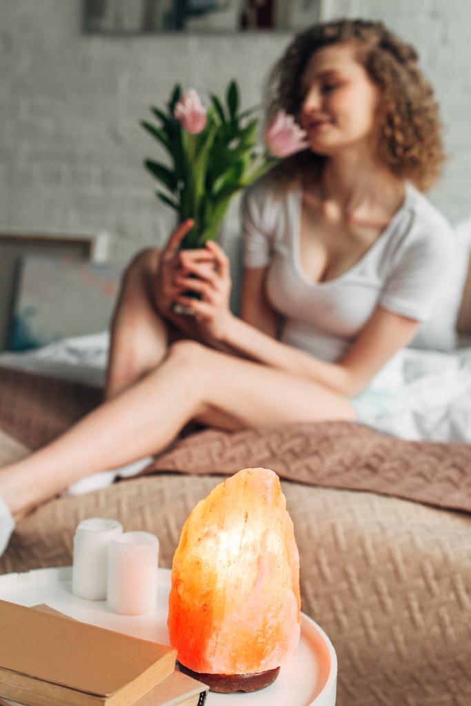 селективное внимание с молодой женщиной, держащей цветы в спальне с гималайской соляной лампой
 - Фото, изображение