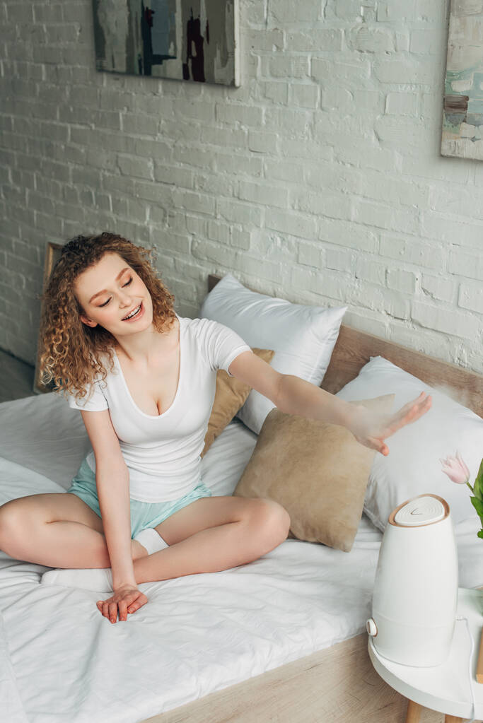 веселая красивая девушка на кровати с очистителем воздуха распространяющим пар
 - Фото, изображение