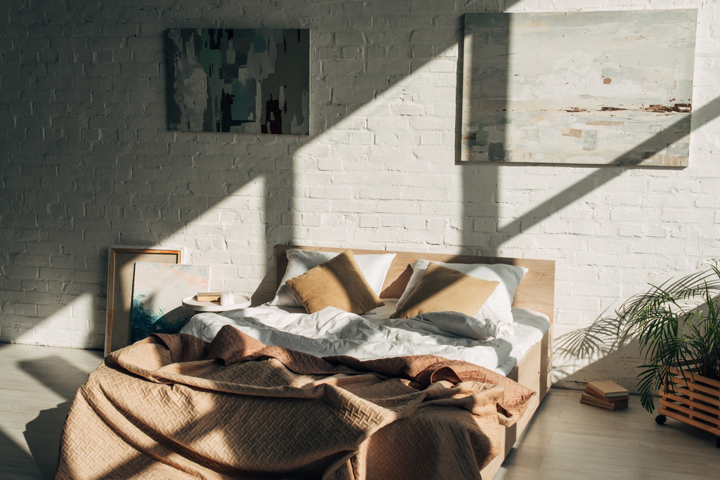slaapkamer interieur met bed, kussens en schilderijen in zonlicht met schaduwen - Foto, afbeelding