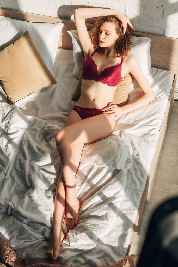 atractiva chica sexy en lencería roja en el dormitorio con luz solar y sombras
 - Foto, imagen