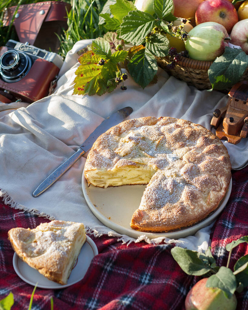 Пикник на траве с яблочным пирогом, яблоки в корзине на клетчатом одеяле
. - Фото, изображение