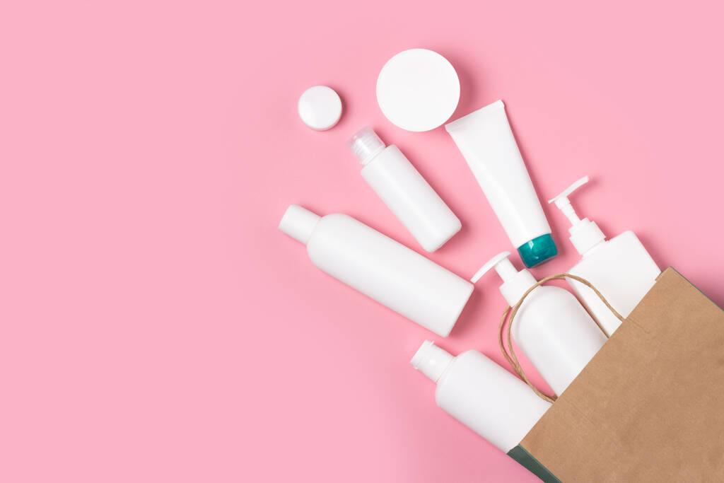 Frascos cosméticos blancos caen de una bolsa de compras sobre un fondo rosa. Compra de cosméticos y productos de higiene, compras a domicilio
 - Foto, Imagen