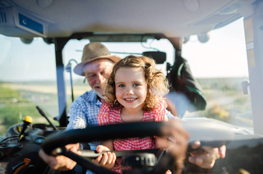 Ανώτερος αγρότης με μικρή εγγονή που κάθεται σε τρακτέρ, οδηγώντας. - Φωτογραφία, εικόνα