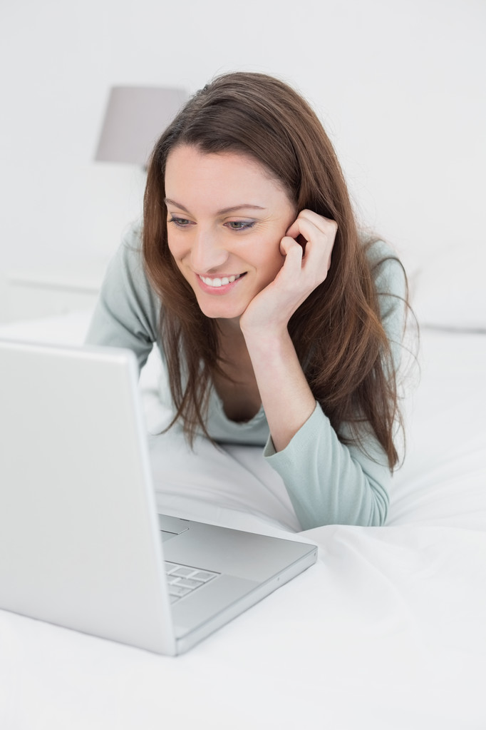 Feliz relajada mujer casual utilizando el ordenador portátil en la cama
 - Foto, imagen
