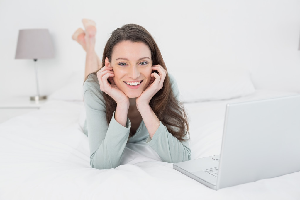 Femme décontractée souriante décontractée avec ordinateur portable au lit
 - Photo, image