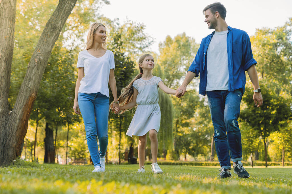 Üç kişilik mutlu beyaz bir aile parkta yürürken birbirlerine bakıyorlar. - Fotoğraf, Görsel