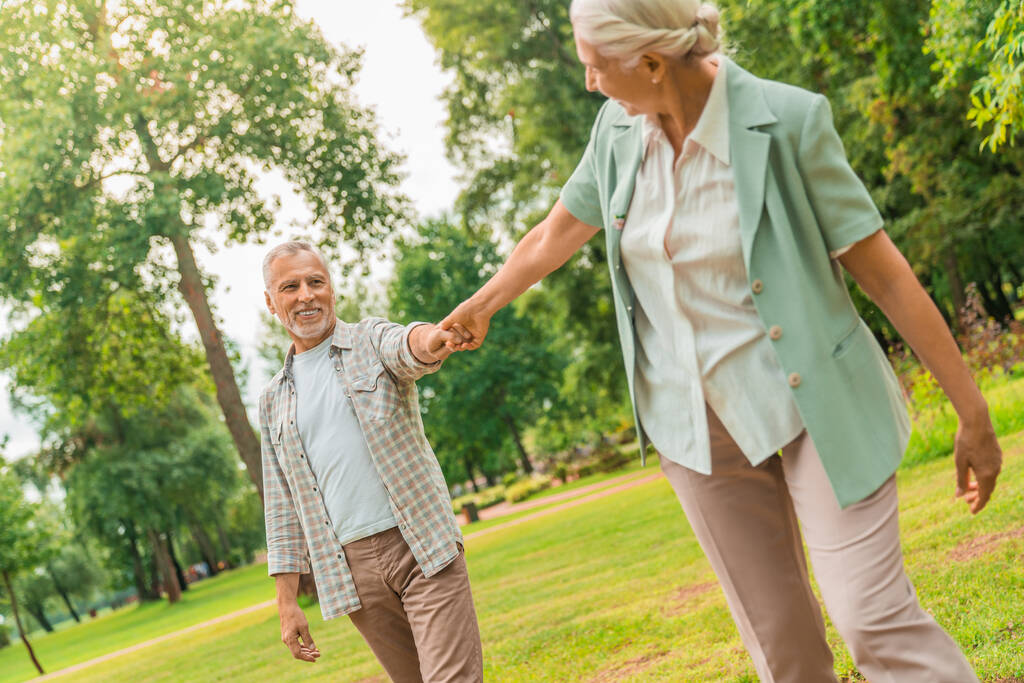 Femme âgée souriante tenant la main de son partenaire et marchant devant à l'extérieur
 - Photo, image