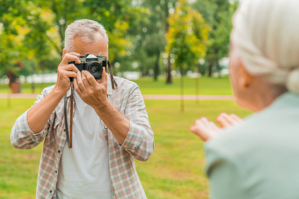 Guapo hombre mayor fotografiando a su esposa por cámara de fotos al aire libre
 - Foto, Imagen