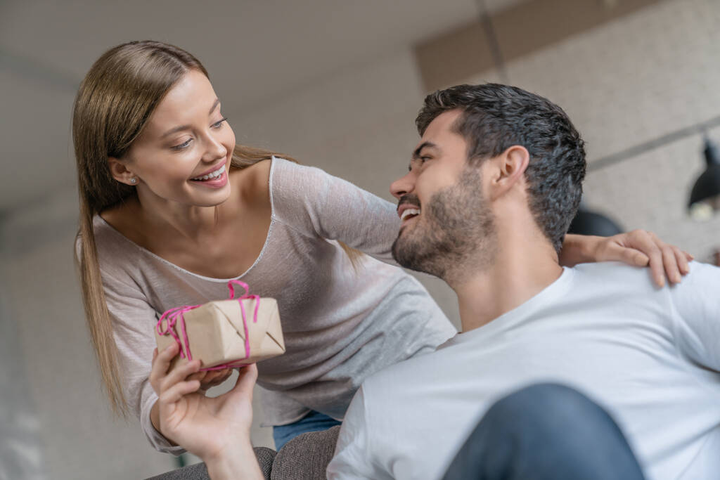 Güzel bir kızın erkek arkadaşına hediye kutusu verirken yakın çekimde, güzel genç bir çift evde kutlama yapıyor.. - Fotoğraf, Görsel