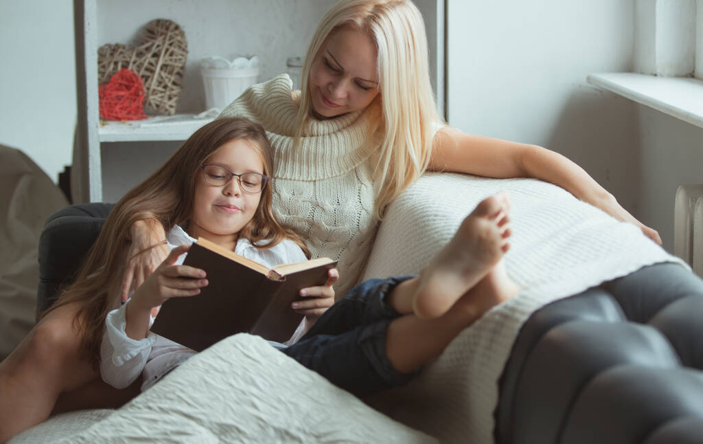 孤独の時代の家族はソファの上の家で本を読む。あなたの家を離れることなく隔離中に自分自身を忙しく保つ方法 - 写真・画像