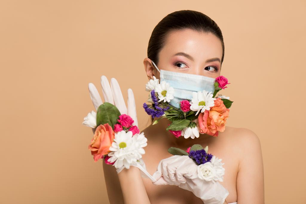 attraktive nackte asiatische Mädchen in floraler Gesichtsmaske tragen Latex-Handschuhe isoliert auf beige - Foto, Bild