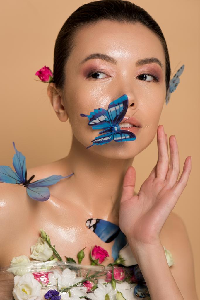 όμορφη γυμνή Ασιάτισσα κοπέλα σε λουλούδια με πεταλούδες στο σώμα απομονώνονται σε μπεζ - Φωτογραφία, εικόνα
