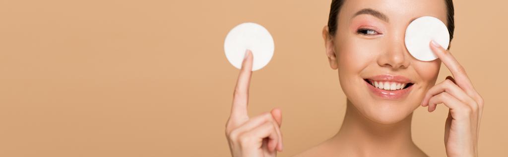 panoramic shot of smiling asian girl removing makeup from face with cotton pads isolated on beige - Photo, Image