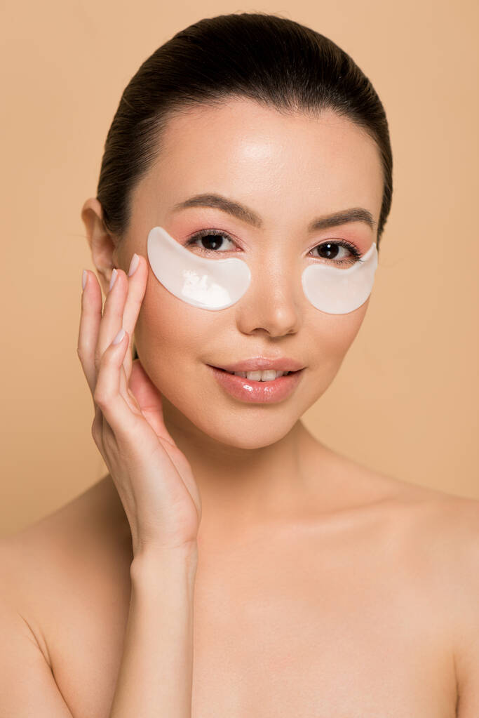 tender nude asian girl with white collagen eye pads isolated on beige - Photo, Image