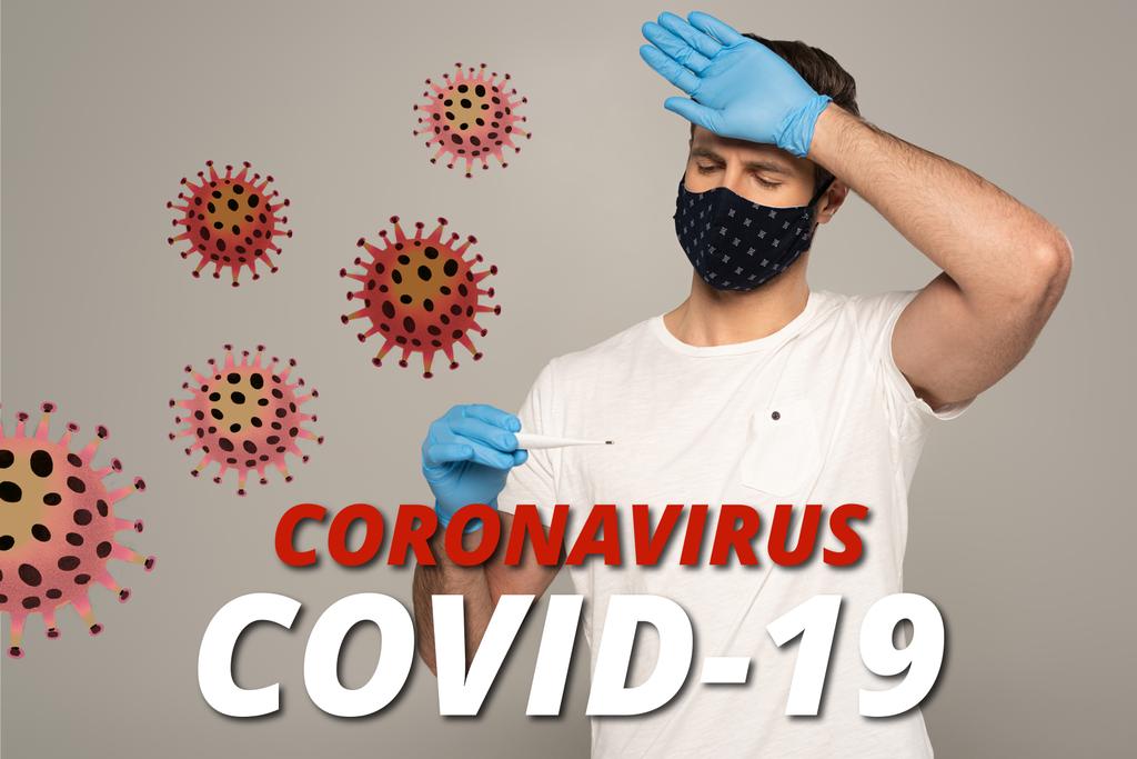 Mężczyzna w masce ochronnej i rękawiczkach lateksowych trzymający termometr i dotykające czoło izolowane na szarym, koronawirusowym wirusie covid-19 i ilustracji bakterii - Zdjęcie, obraz