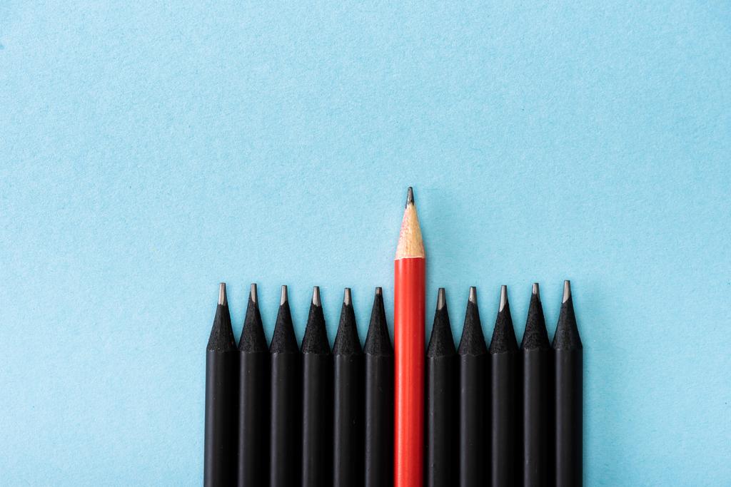 Bovenaanzicht van rood potlood tussen zwart op blauwe achtergrond - Foto, afbeelding