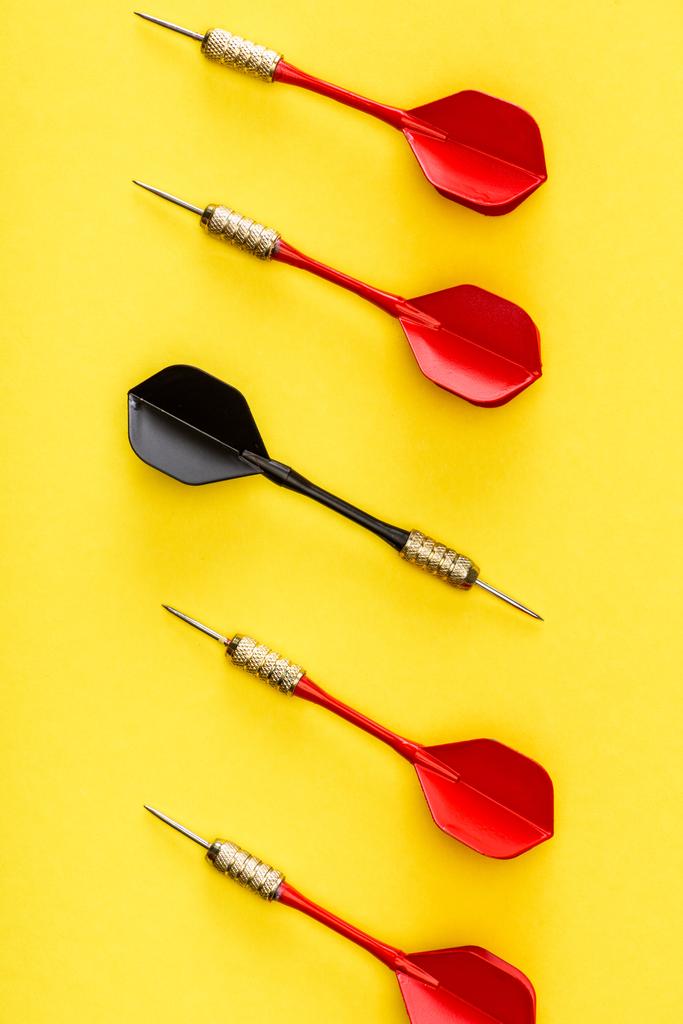 Flat lay with unique black dart among red on yellow - Photo, Image